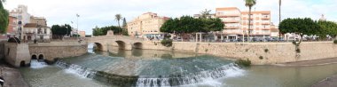 Rojales, Alicante, Spain, October 28, 2024: Great panoramic view of the 1790 Bridge over the Segura River with a Ferris wheel and a dam as it passes through Rojales, Alicante, Spain clipart