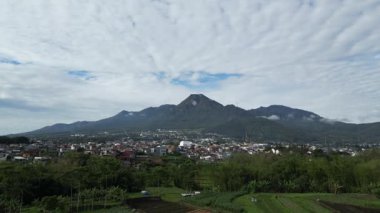 Bulutlu mavi gökyüzü ve aşağıdaki yerleşim alanları ile dağ manzarası