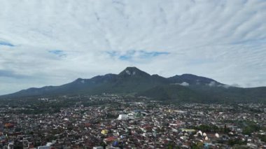 Bulutlu mavi gökyüzü ve aşağıdaki konut binalarıyla dağ manzarası