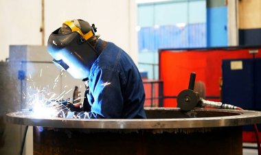 İşçi metal bir parça kaynak yapıyor, güvenlik ekipmanları ile. 