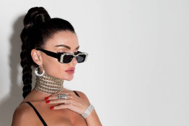 Güneş gözlüğü takan ve uzun at kuyruğu takan bir kadın stüdyoda yakın plan bir portre için poz veriyor. Dikkat çekici görüntüsü dikkat çekiyor.