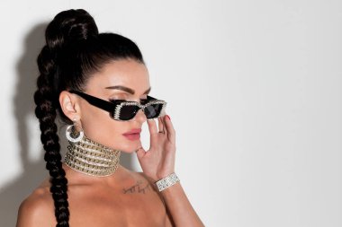 Güneş gözlüğü takan şık bir kadının yakın plan portresi ve şık bir at kuyruğu, stüdyoda zarif ve kendine güvenen bir poz, büyüleyici varlığı,