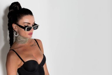 Büyüleyici yakın plan bir portrede, güneş gözlüklü ve parlak at kuyruklu bir kadın stüdyoda özgüven ve cazibeyle poz veriyor, göz kamaştırıcı atmosferi parlıyor.