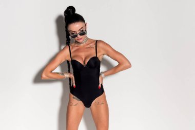 Çekici ve çekici, gergin vücutlu ve uzun at kuyruklu ince bir kadın, stüdyonun sıcak renklerine güven ve şehvet saçan siyah iç çamaşırlarıyla kışkırtıcı bir şekilde poz veriyor.