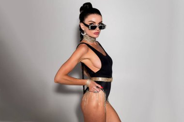 İnce fiziği ve çekici uzun saçları olan zarif bir kadın. Şık siyah iç çamaşırlarıyla baştan çıkarıcı poz veriyor. Hafif stüdyo ışıklarıyla aydınlatılıyor.