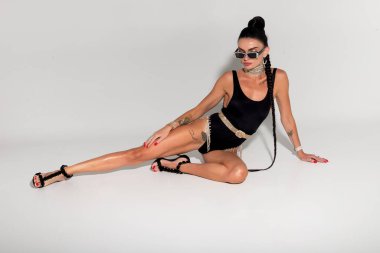 Kendine güveni ve cazibesi ile narin bir bayan büyüleyici siyah iç çamaşırlarıyla stüdyo zemininde büyüleyici bir poz verirken, zarif at kuyruğu sahnenin cazibesini artırıyor.