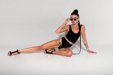 Stüdyoda şehvetli bir şekilde poz veren ince bir kadın siyah iç çamaşırlarıyla, gergin vücuduyla ve dalgalı at kuyruğuyla büyüleyici bir kompozisyon yaratıyor.