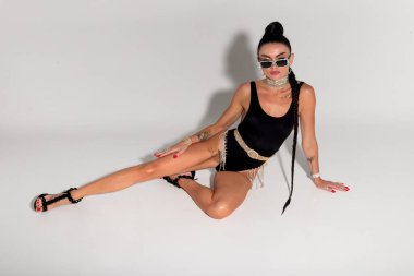 Zarif ve dengeli bir manken, stüdyo zemininde poz verirken şık siyah iç çamaşırı ve gergin fiziğini sergiliyor. Uzun at kuyruğu arkasında zarifçe kıvrılıyor.