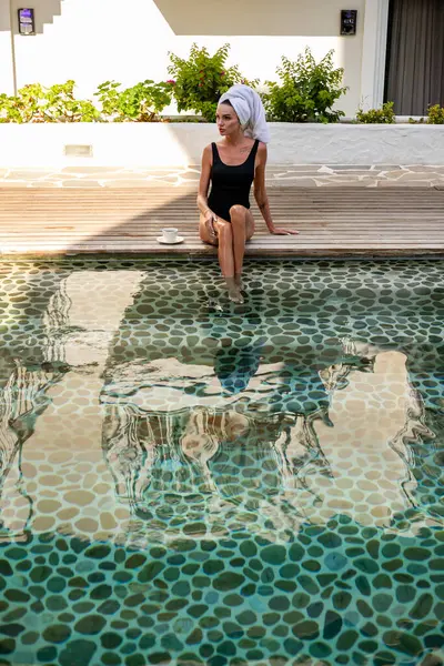 Huzur dolu bir anda, bronz tenli çarpıcı bir kadın sabah kahvesinin tadını pahalı bir villanın havuz kenarında çıkarıyor. Modaya uygun siyah bir mayo giyip kafasında beyaz bir havluyla güzellik ve zarafet yayıyor.
