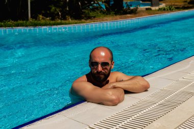 Havuz başı şıklığı: Güneş gözlüklü çekici bir genç poz vererek yüzme havuzunun atmosferine karmaşıklık katıyor