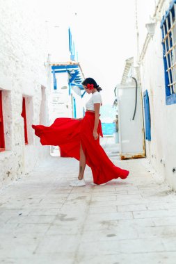 Güneşli kaçış: Kırmızı yaz elbisesi içinde esmer bir kadın, Yunan villalarıyla beyaz bir duvar arkasında poz vererek seyahat ruhunu anımsatıyor.