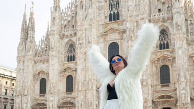 Şık bir keşif: Beyaz kürklü gülümseyen genç bir kadın Milan 'ın güzelliğini kucaklayarak görkemli Milan Katedrali önünde poz veriyor