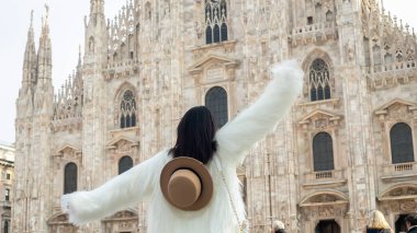 Şehir cazibesi: Işıl ışıl bir turist kız Milano Katedrali önünde zarifçe poz veriyor, beyaz kürkü şehir manzarasıyla çok uyumsuz.