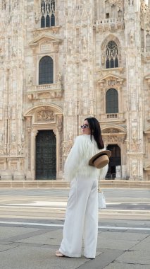 Şehir keşfi: Havalı bir turist kız Milano 'da mutlu bir şekilde gülümsüyor, beyaz kürkü Milan Katedrali' nin sahnesine cazibe katıyor..
