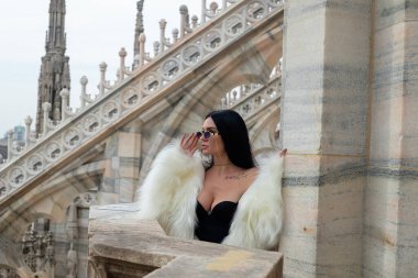 Gökyüzü yüksek zarafet: Şık bir genç kadın, şehrin ufuk çizgisini tamamlayan beyaz kürkü ile Milano Katedrali 'nin çatısında zarifçe poz veriyor.