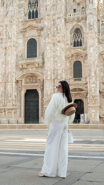 Şehir keşfi: Havalı bir turist kız Milano 'da mutlu bir şekilde gülümsüyor, beyaz kürkü Milan Katedrali' nin sahnesine cazibe katıyor..