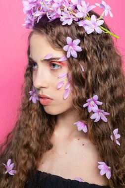 Mor çiçeklerin yumuşak renkleriyle tamamlanan karmaşık bukleler, çiçekli bir dokunuşla kızın cazibesini arttırıyor..