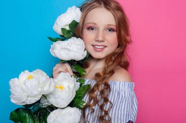 Sevimli genç kız, narin beyaz çiçeklerle çevrili, yüzü pembe bir zemine karşı neşeli bir jestle gizlenmiş. Tatlı ve masum kavramlar için mükemmel..