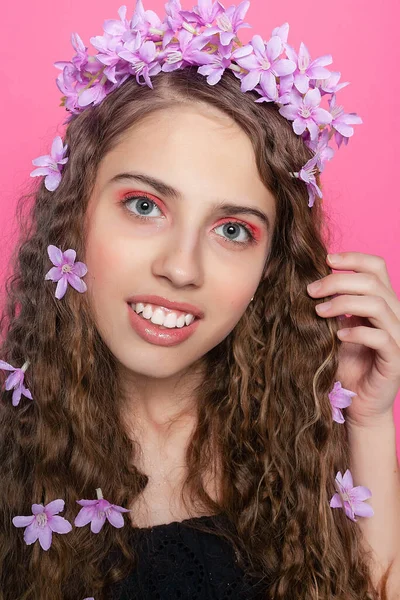 Curly-haired enchantress dons purple blossoms, enhancing her natural beauty with a touch of floral elegance and whimsy.
