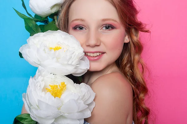 Captivating portrait of a young girl surrounded by white blossoms, her face hidden in a playful manner against the gentle pink backdrop. Ideal for greeting cards and posters