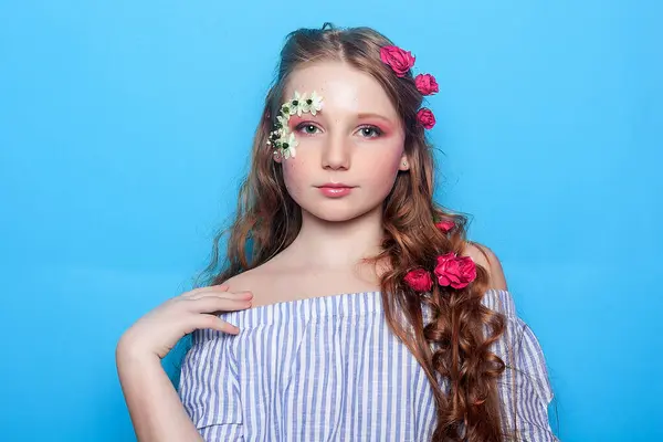 快乐的小女孩装饰着雏菊 她的脸在充满活力的蓝色背景下闪闪发光 流露出喜悦和纯真 完美的春季主题设计 图库图片