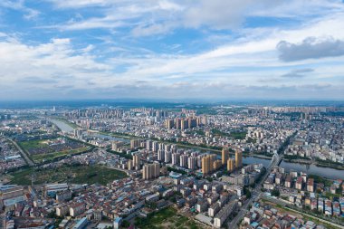 Ufuk boyunca uzanan genişleyen bir şehir beyaz bulutlu mavi bir gökyüzünün altında.