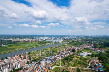 Suizhou Çin 'in panoramik manzarası, yemyeşil tarım arazileri ve parlak bir gökyüzü altındaki dağınık binalar arasında kıvrılan sakin nehri ortaya çıkarıyor..