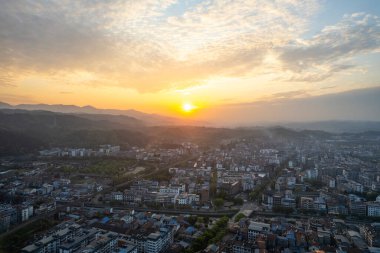 Çin 'deki Wudang kasabasını birçok binayla kaplayan hava manzaralı dağlara karşı sıcak günbatımı ışığı banyosu yapar..
