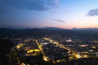 Çin 'in aydınlık Wudang kasabası, akşam alacakaranlık gökyüzünün altındaki görkemli dağların arasına kurulmuş parlak ışıklarını sergiliyor..