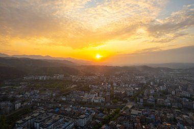 Çin 'in Wudang kasabası, altın günbatımı binaları ve uzak dağları aydınlatırken yukarıdan geniş bir şehir manzarası sunuyor..