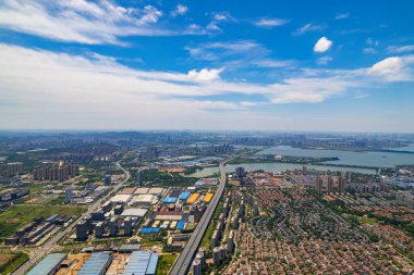 Wuhan, Çin 'deki Jiangxia Bölgesi' nin hava manzarasında geniş şehir binaları, yolları birleştiren yollar ve parlak bir gökyüzü altında huzurlu bir göl sergileniyor..