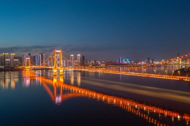 Köprü, gece nehrini aydınlatıyor. Şehir ışıkları suya yansıyor..