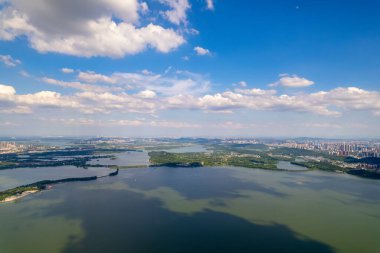 Geniş göl, Çin 'deki Wuhan şehrine doğru uzanan bulutlarla gökyüzünü yansıtır..