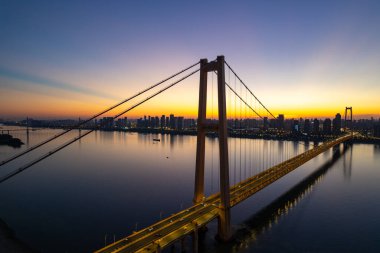 Güzel bir günbatımında gökyüzü aydınlanırken, büyük bir köprü sakin bir nehir boyunca uzanır..