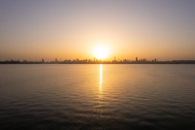 Gölün üzerinde gün doğumu yansıtan şehir silüeti.