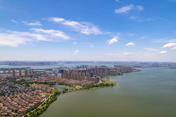 Китай Ухань разворачивается вдоль широкой зеленой воды под ярко-голубым небом с пушистыми белыми облаками.
