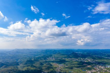 Guizhou Çin manzarası uçsuz bucaksız mavi gökyüzünün altında beyaz bulutlu, yuvarlanan yeşil tepeleri ve dağınık köyleri gösteren bir manzara..