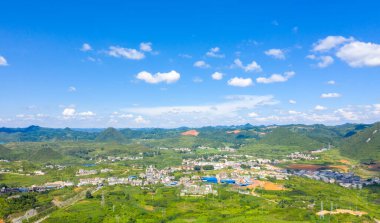 Guizhou Çin 'in geniş bir görüntüsü yeşil yuvarlanan tepeleri ve mavi gökyüzünün altında dağınık bir köyü gösteriyor..