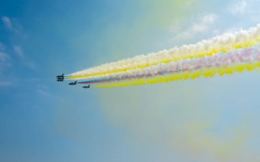 Pek çok jet, açık mavi gökyüzünde çarpıcı bir hava görüntüsü bırakarak, renkli dumandan izler bırakarak diziliş halinde uçar..