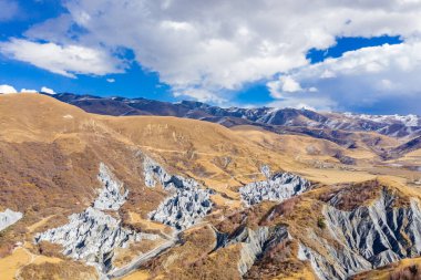 Çin 'in batı bölgesi dağları beyaz bulutlu mavi gökyüzünün altında dramatik kaya oluşumları sergiliyor..