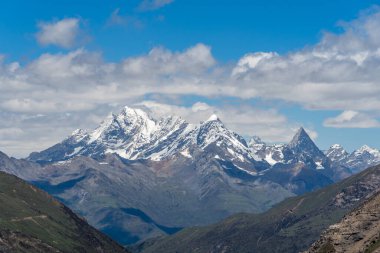 Uçsuz bucaksız Sichuan bölgesinde, parlak mavi bir gökyüzünün altında, dağılmış bulutlarla karlı zirveler yükseliyor. Dağlık arazinin doğal güzelliğini gözler önüne seriyor..