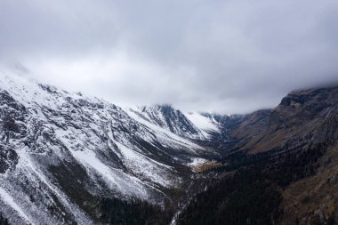 Aralarına derin bir vadi oyulmuş, karlı dağlar arazide uzanır. Bulutlar alçaktan sarkır, engebeli araziye yumuşak bir ışık saçar. Ağaçlar daha alçak yamaçlara nokta koyarlar, koyu formları beyaz karla çelişir. Uçsuz bucaksız, açık uzay...