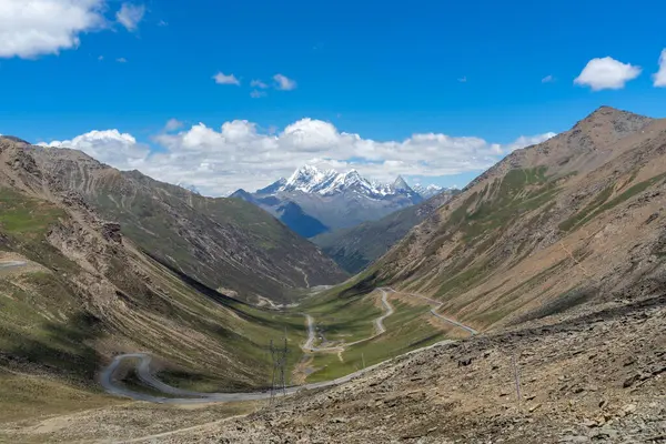 Çin Sichuan bölgesi dağ yolu yeşil vadileri geçerek mavi gökyüzünün altındaki karlı zirvelere doğru ilerliyor..