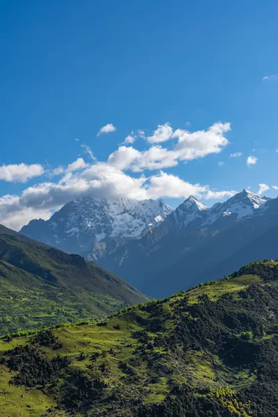 Çin 'in uçsuz bucaksız yamaçlarında Sichuan bölgesi bulutlu mavi gökyüzü altında, yeşil vadiler ve kar tepeleri sergiliyor..