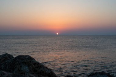 Yunanistan 'ın Girit adasında denizin üzerinde çarpıcı bir gün doğumu. Sakin sular, sabah gökyüzünün altın renklerini yansıtıyor. Huzurlu bir deniz manzarası oluşturuyor..