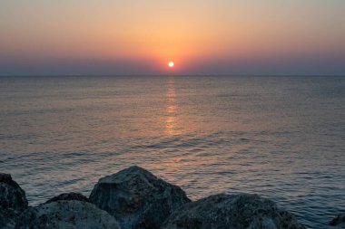 Yunanistan 'ın Girit adasında denizin üzerinde çarpıcı bir gün doğumu. Sakin sular, sabah gökyüzünün altın renklerini yansıtıyor. Huzurlu bir deniz manzarası oluşturuyor..