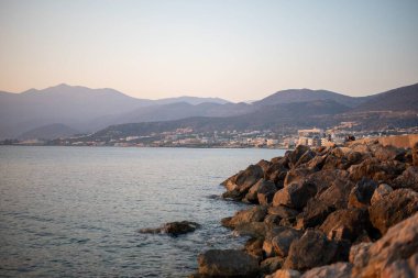 Hersonissos, Girit 'te tekneli bir sahil sahili manzarası. Huzurlu sular, adanın doğal güzelliği tarafından çerçevelenmiş büyüleyici kasabayla buluşur..