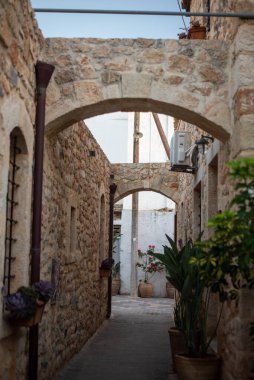 Narrow Greek streets in Hersonissos, Crete, Greece, lined with charming whitewashed buildings, colorful flowers, and vibrant local shops, exuding charm. clipart