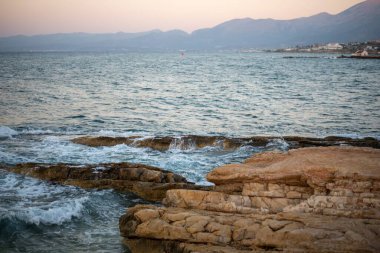 A beach with fine golden sand, gentle waves lapping at the shore near the city of Hersonissos on the island of Crete, Greece. clipart