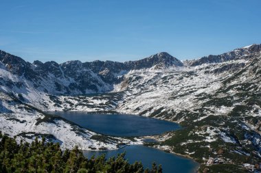 An unparalleled view of a crystal-clear lake in the Valley of Five Ponds, Tatra Mountains, Poland, reveals stunning alpine beauty, surrounded by rugged peaks and lush greenery clipart